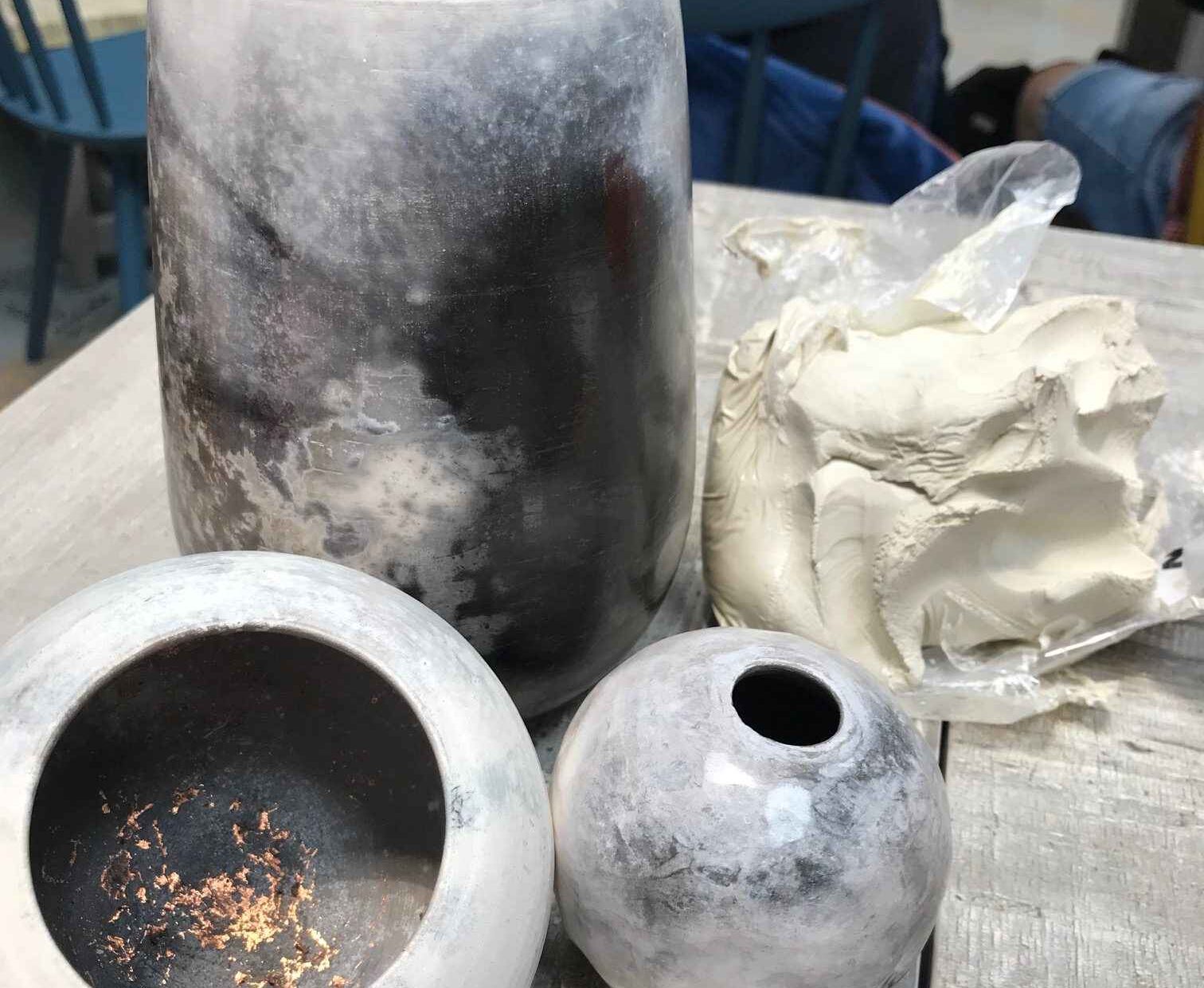 Three of Ian's pots next to a lump of white clay. The pots are all have random colouring of grey, white and black achieved from a smoking process.