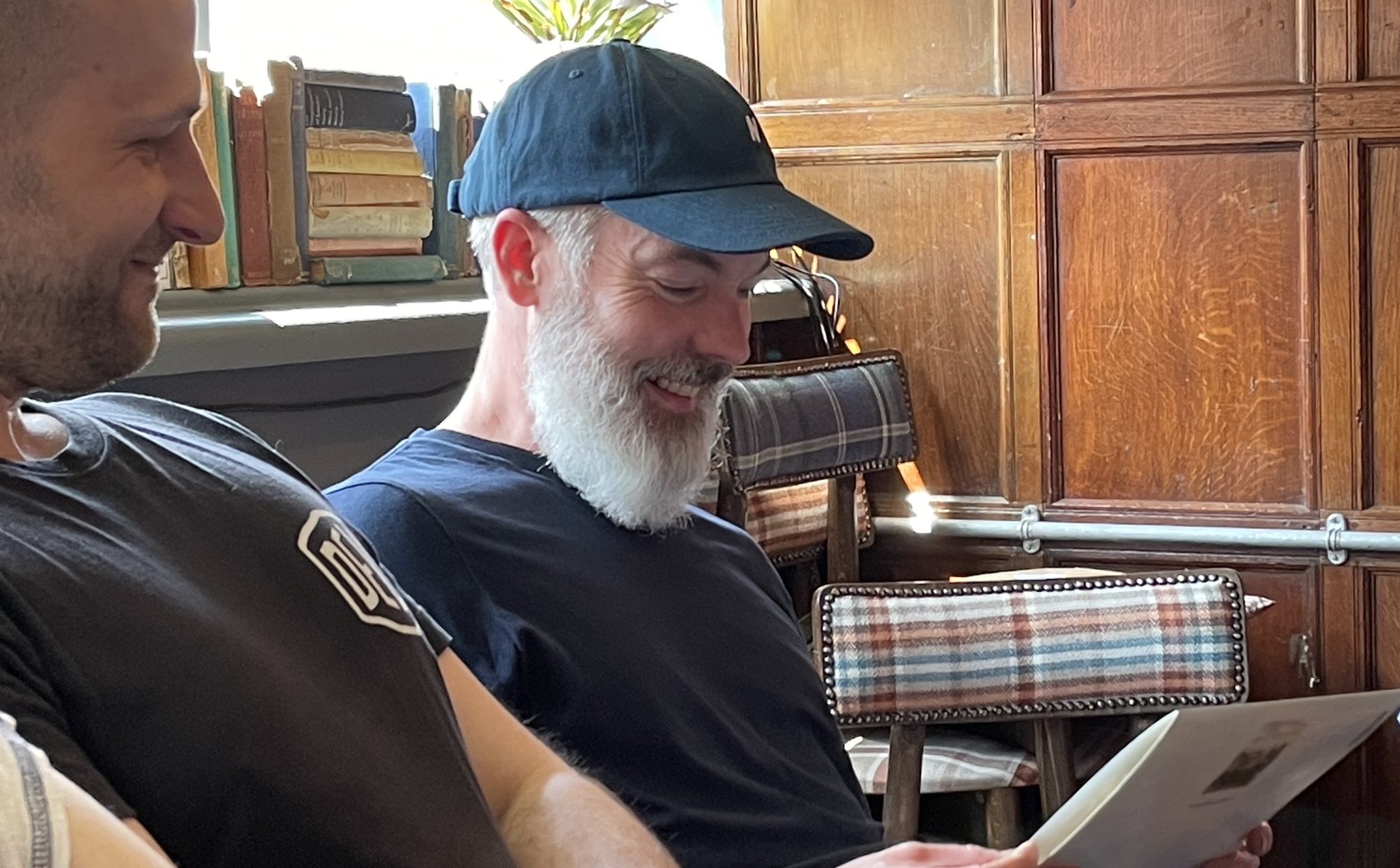 Ian in a navy blue t-shirt and cap is smiling and looking down at his A4 sized card. 