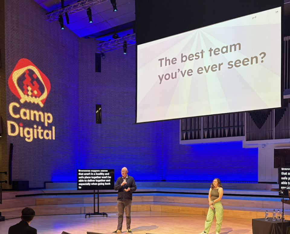 A man and a woman on stage, above them a screen says the best team you've ever seen? 