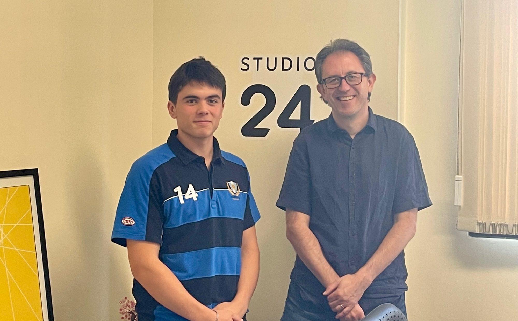 In the office, Ben stands with MD Simon Jones in front of the Studio 24 logo.