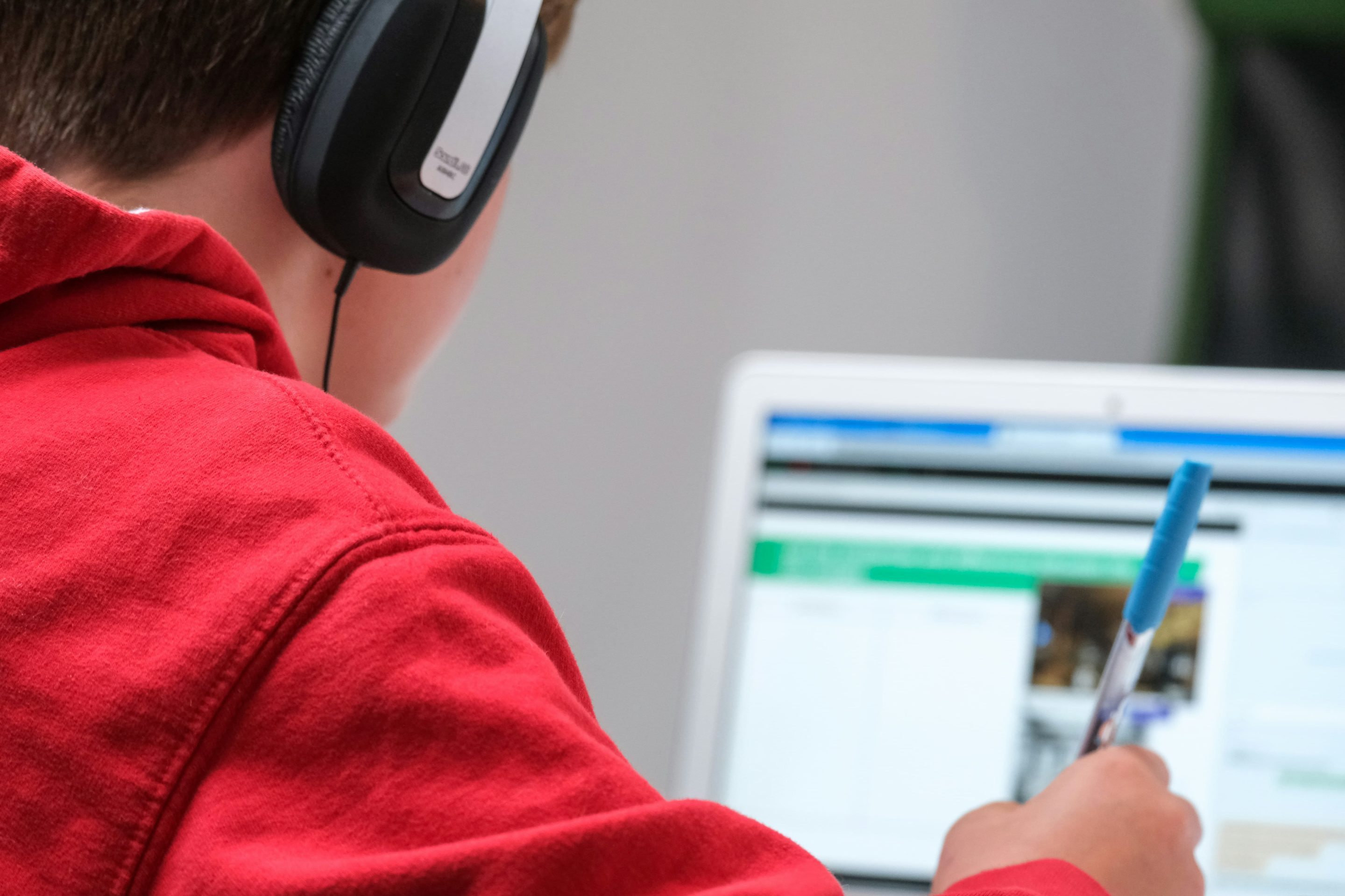 A young student wearing headphones listens to a screen reader while browsing a web page on their laptop.