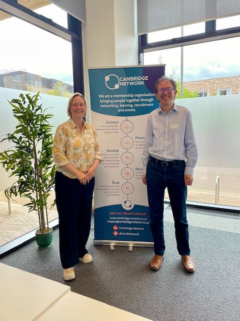 A man and a woman stand by a pull up banner about Cambridge Network, a membership organisation bringing people together through networking, learning, recruitment and events.
