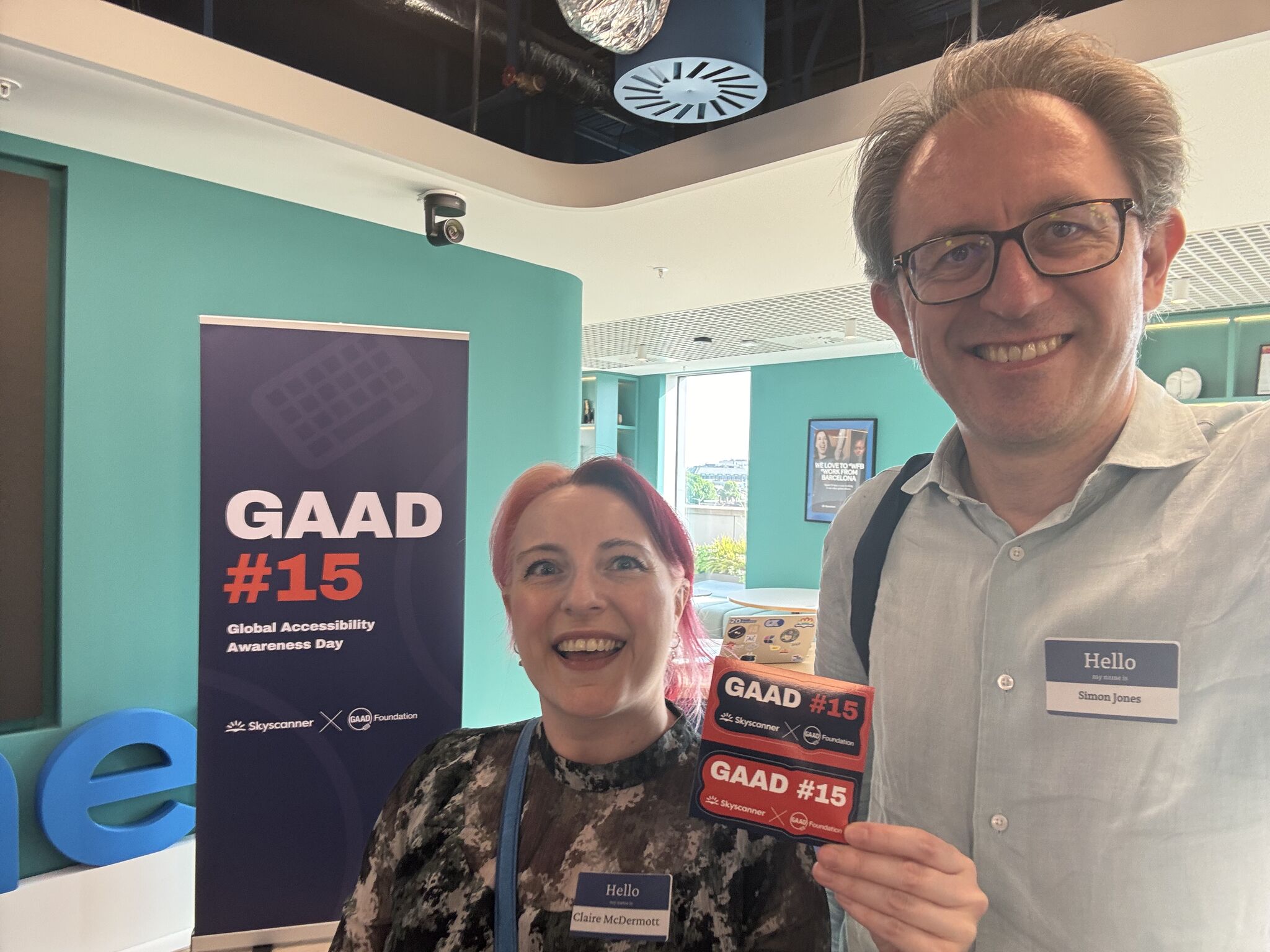 A man and a woman stand in front of a GAAD 15 pull up poster. The woman is holding a GAAD 15 flyer.