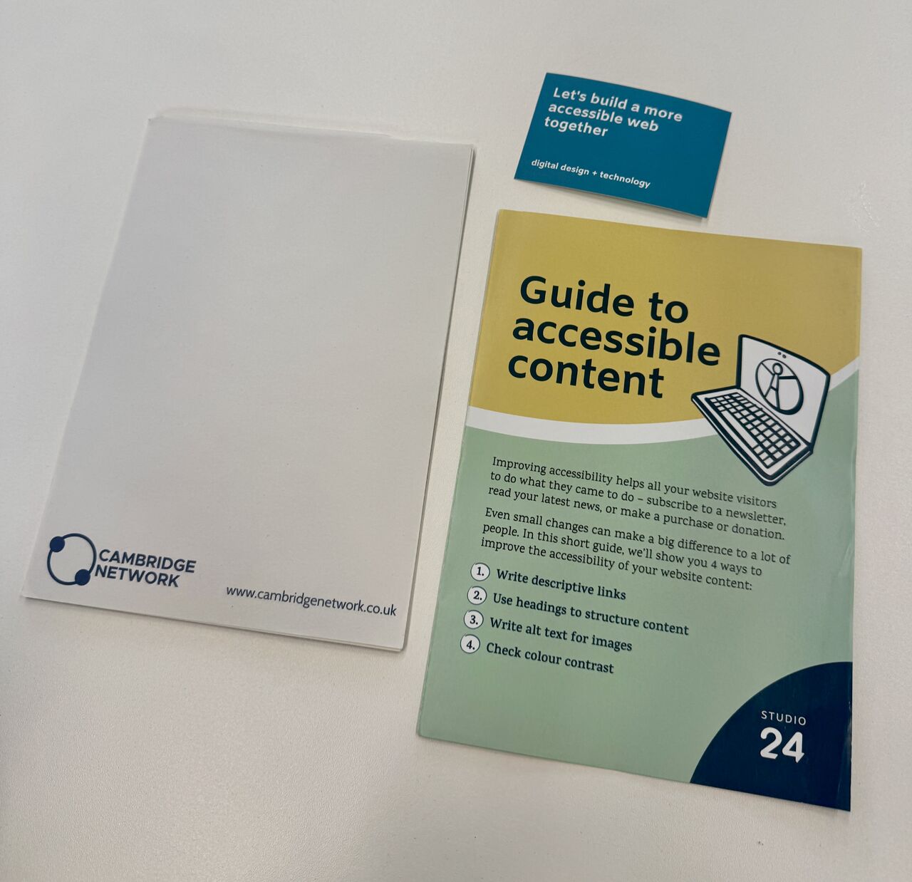 A Cambridge Network branded notepad, a guide to accessible content and a business card that reads: Let's build a more accessible web together.