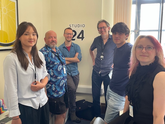 In an office, standing by the Studio24 logo are 4 men and 2 women